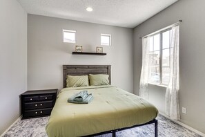 A bedroom with a bed, a nightstand, a window with curtains, and two wall-mounted picture frames.