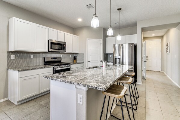 A modern kitchen with white cabinets, granite countertops, stainless steel appliances, and pendant lighting.