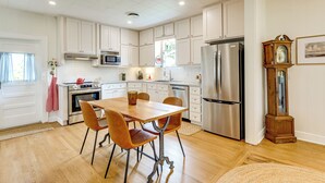 Una cocina con armarios blancos, electrodomésticos de acero inoxidable, una mesa de comedor de madera con sillas y un reloj de pie.