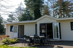 A single-story building with a patio area featuring a table and chairs, sliding glass doors, and a small garden. - Holiday home in Lochem with terrace (Lochem)