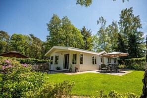 A single-story house with a covered patio, a lawn, and surrounding trees.
