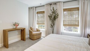 Ein Schlafzimmer mit einem großen Bett, einem Holzkonsolentisch, einem Stuhl und einem Fenster mit Vorhängen.