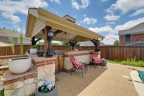 Eine Terrasse im Freien mit überdachter Grillgelegenheit, Stein- und Backsteinmauern sowie Gartenmöbeln.