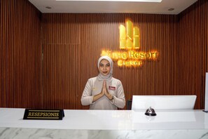 A reception desk with a 'RESEPSIONIS' sign, a woman standing with hands in a prayer position, and a 'Nimo Resort' sign in the background.