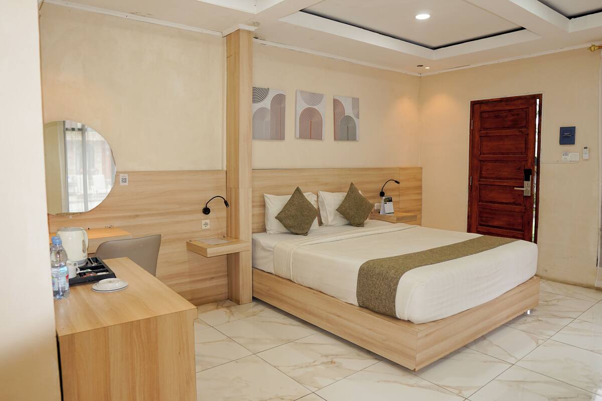 A hotel room with a bed, bedside table, lamp, and a desk with a chair.