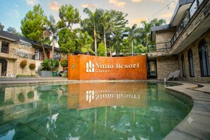 A swimming pool with a wooden sign reading 'Nimo Resort' and 'Cater'.