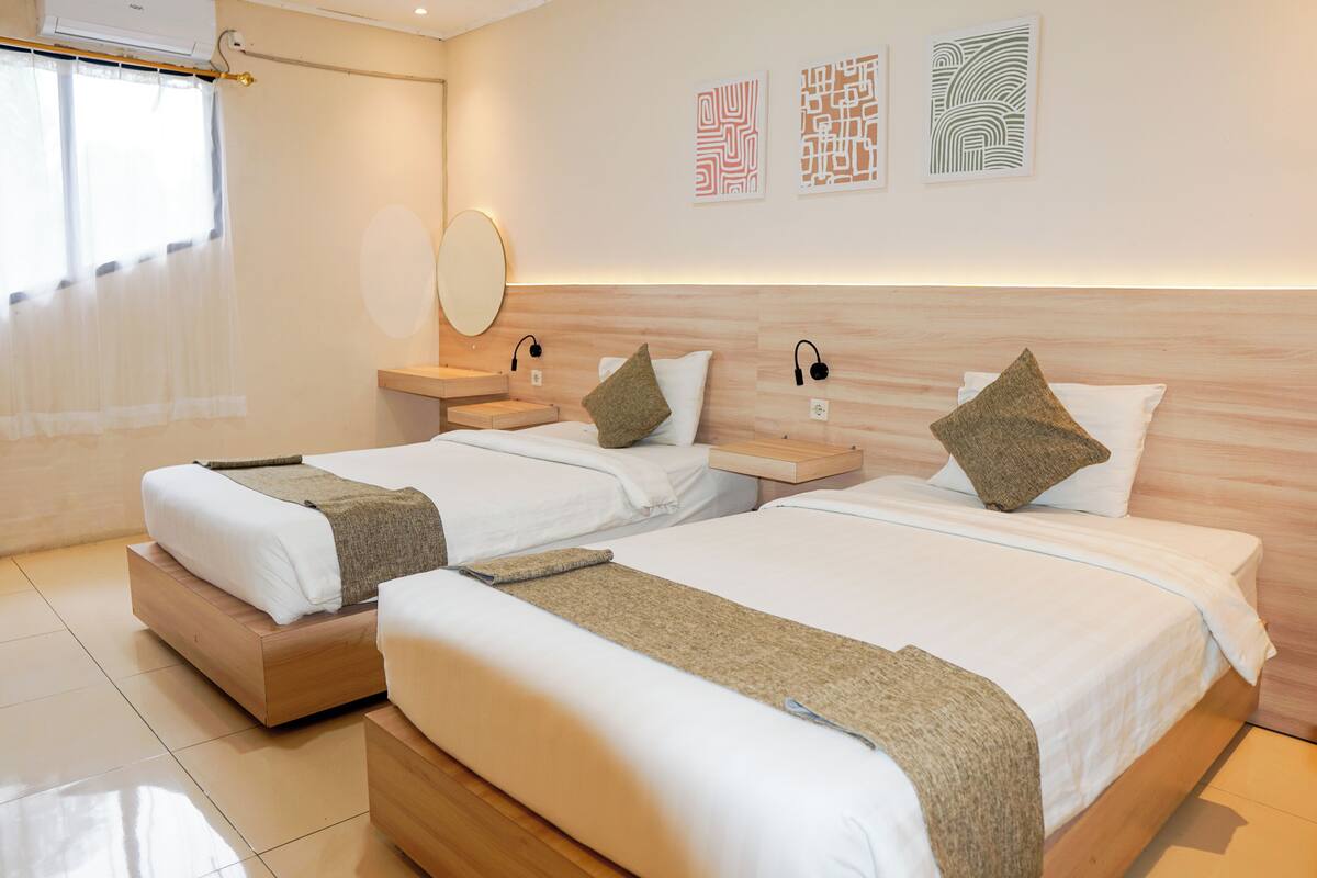 A hotel room with two beds, a bedside table, a mirror, and wall art.