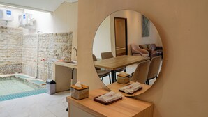 A hotel room with a stone wall, a wooden reception desk, a mirror, a pool, and a dining area. - Nimo Resort Ciater (Ciater)