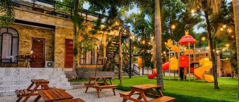 A courtyard with picnic tables, a play area with slides, and a building with a brick facade.
