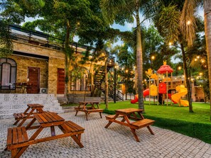 A courtyard with picnic tables, a play area with slides, and a building with a brick facade. - Nimo Resort Ciater (Ciater)