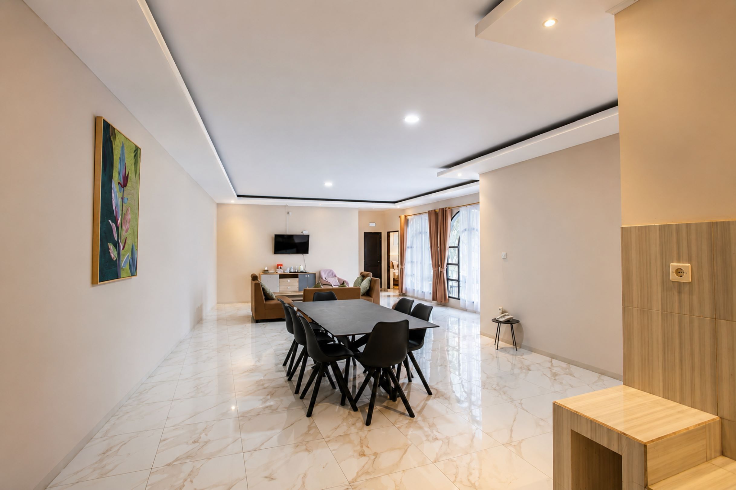 A spacious room with a dining table, chairs, a sofa, and a TV mounted on the wall.