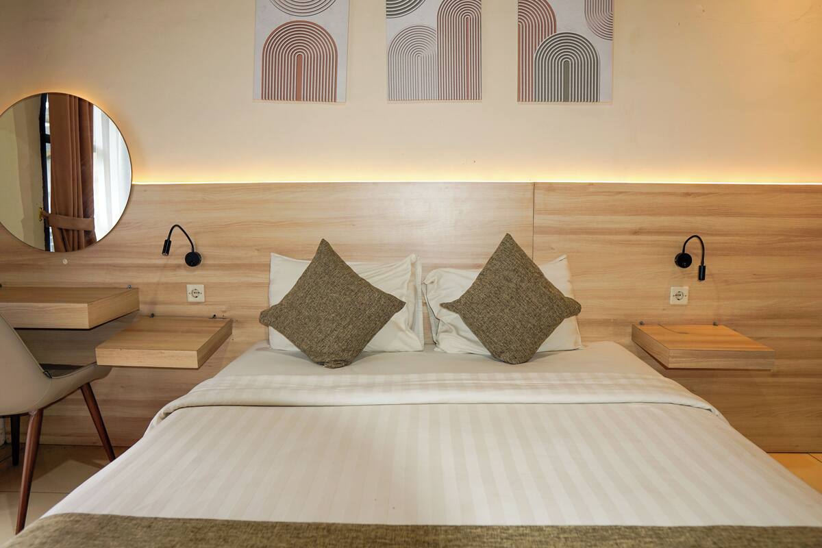 A neatly arranged hotel room with a bed, bedside tables, a chair, a mirror, and wall art.