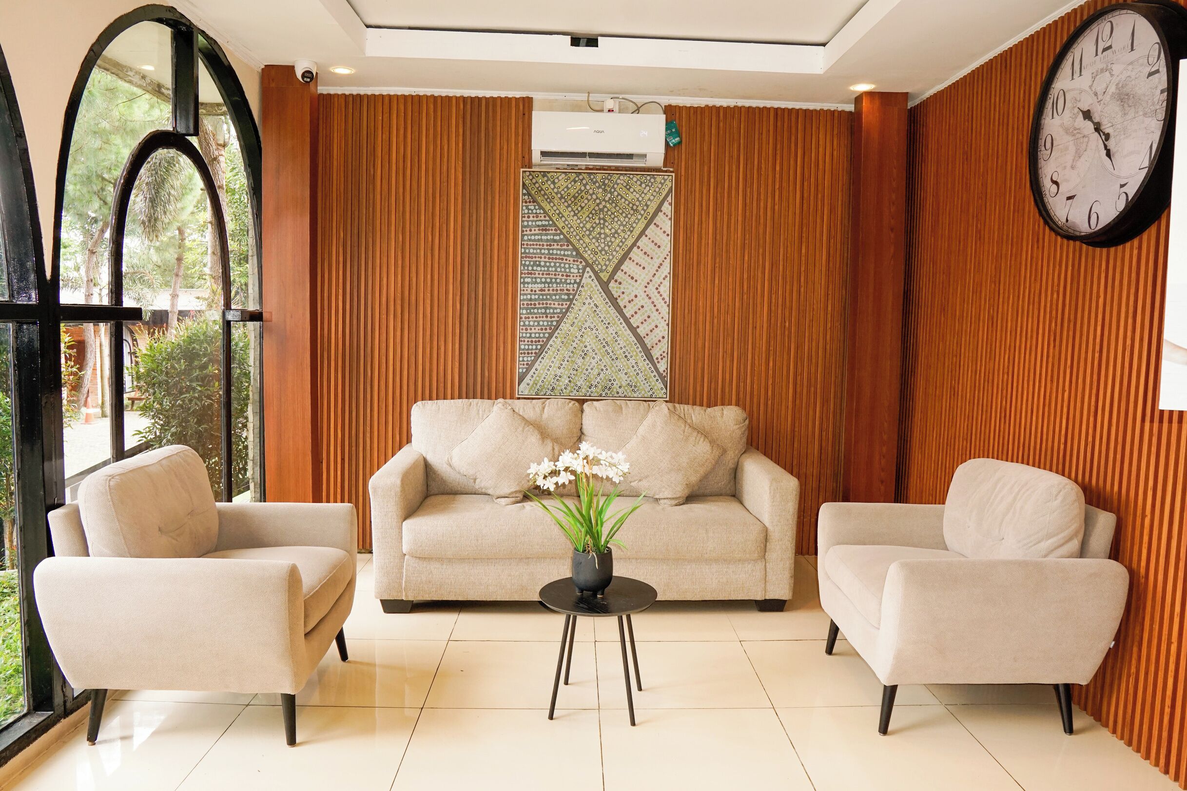 A modern living room with a sofa, two armchairs, a coffee table, and a large wall clock.