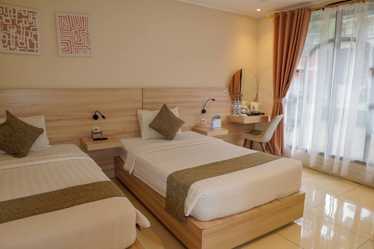 A hotel room with two beds, a desk, a chair, a mirror, and a window with curtains.