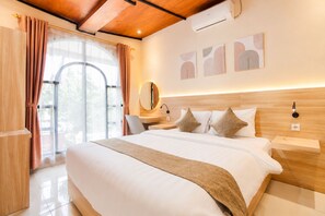 A hotel room with a large bed, wooden headboard, a desk with a chair, a mirror, and artwork on the wall.