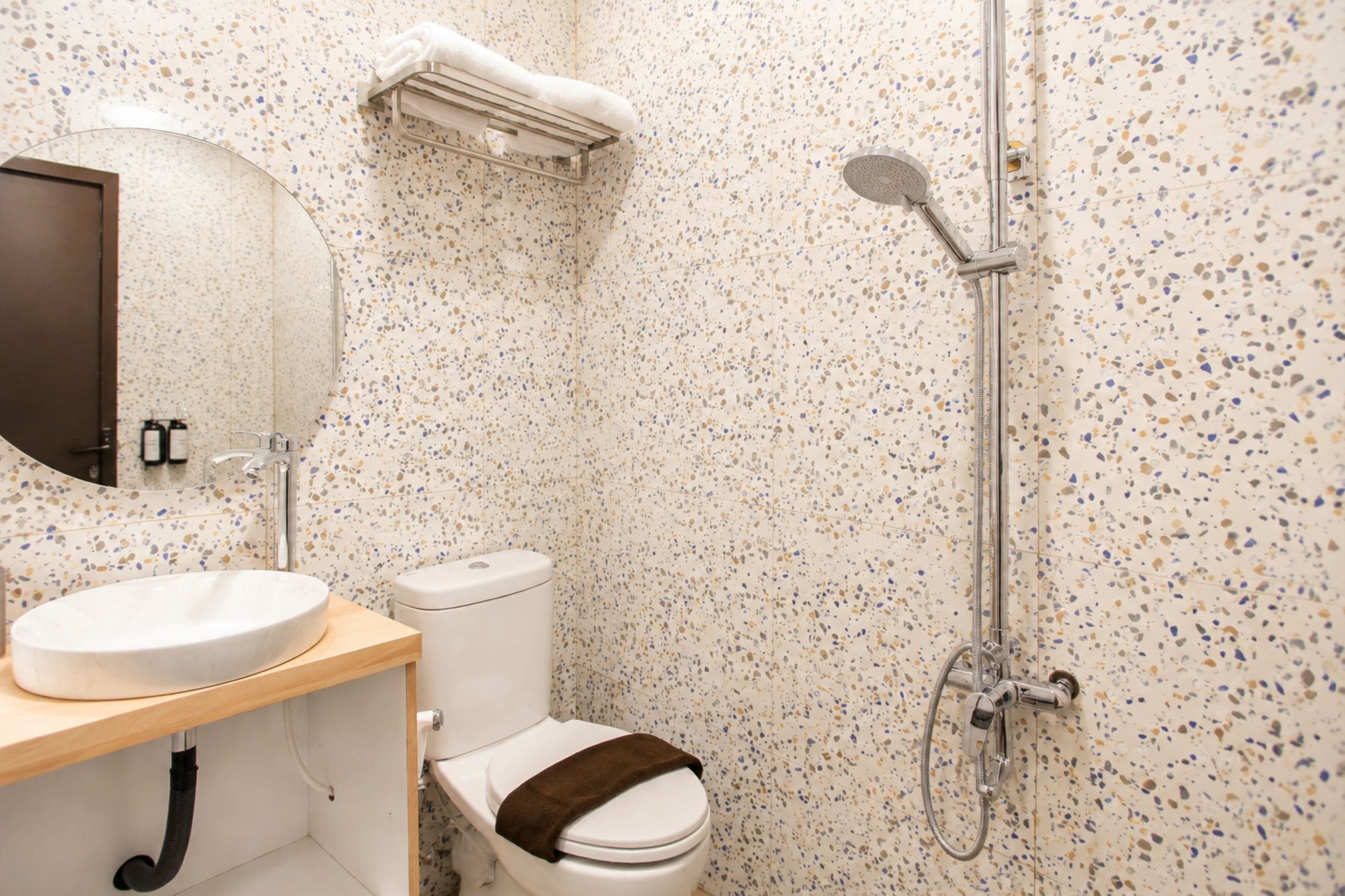 Baño con lavamanos redondo, inodoro y ducha con cabezal de ducha de mano.