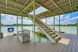 Eine Holzterrasse mit einer Treppe zu einem Steg, einem Stuhl und einem Kajak.