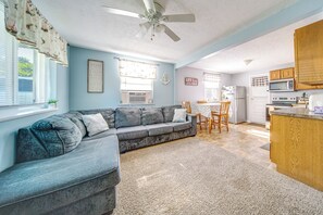 A living room with a gray sectional sofa, a ceiling fan, and a kitchen area with wooden cabinets and appliances. - Steps to Strip & Lake! Family-Friendly Geneva Gem (Geneva)
