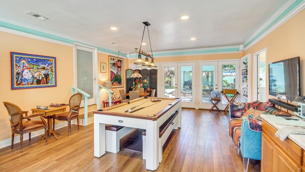 A pool table, chairs, a television, and artwork in a room with wooden floors and a door leading outside. - Heron House - Beach, Fishing Pier, Boat Launch (Bay St Louis)
