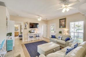 A living room with a sofa, ottoman, and a TV. There is a dining area with a table and chairs.
