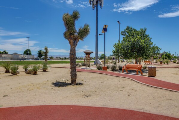 Un parque con un camino rojo, bancos y una palmera.