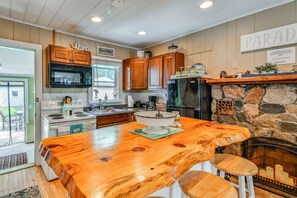 A kitchen with wooden cabinets, a stone fireplace, a large island with stools, and a view of the outdoors.