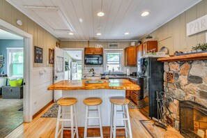 A kitchen with a central island, wooden bar stools, a stone fireplace, and a sign reading 'Welcome Cottage.' - George Lake Escape! Charming 1950s Cabin (Lupton)