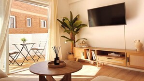 Ein Wohnzimmer mit einem runden Tisch, einem Fernseher, einer Pflanze und einem Balkon mit Tisch und Stühlen.