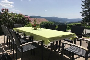 Ein Essbereich im Freien mit Tisch und Stühlen, umgeben von Grün und Blick auf ferne Hügel.