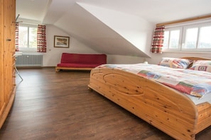 Ein Schlafzimmer mit Schräge, einem hölzernen Bett, einem roten Sofa und einem Fenster mit Vorhängen.