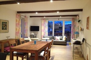 A dining area with a wooden table and chairs, a sofa, and a television. - Holiday apartment with 1 bedroom (Garmisch-Partenkirchen)