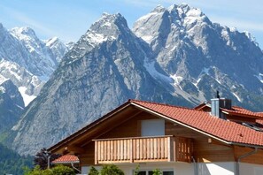 A mountain cabin with a red-tiled roof, wooden balcony, and a view of snow-capped peaks. - Holiday apartment with 1 bedroom (Garmisch-Partenkirchen)