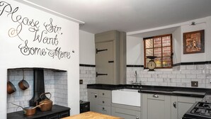 A kitchen with a black stove, white cabinets, a wooden bench, and a decorative wall with text. - 2 bedroom accommodation in Broadstairs (Broadstairs)