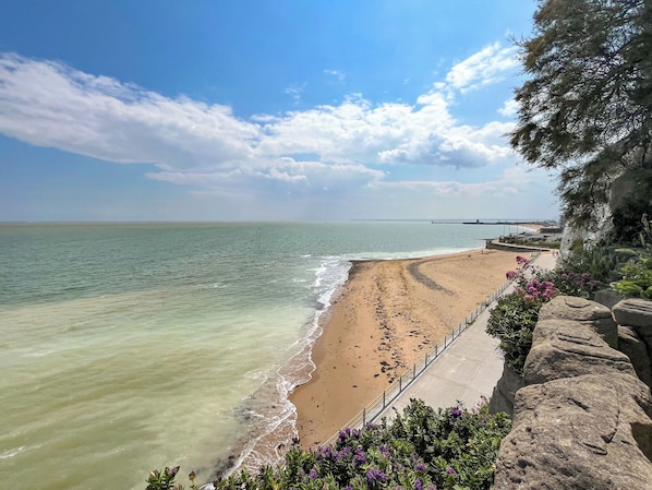 Ein Strand mit klarem Wasser, sandigem Ufer und einem felsigen Klippenhang mit Vegetation.