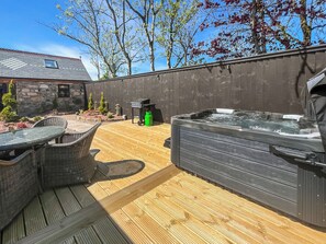 Eine Holzterrasse mit Whirlpool, Korbmöbeln und einem Grill.