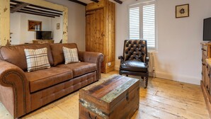 A living room with a brown leather sofa, a wooden chest, and a black leather armchair. - Pickwick's Place - UK51958 (Broadstairs)