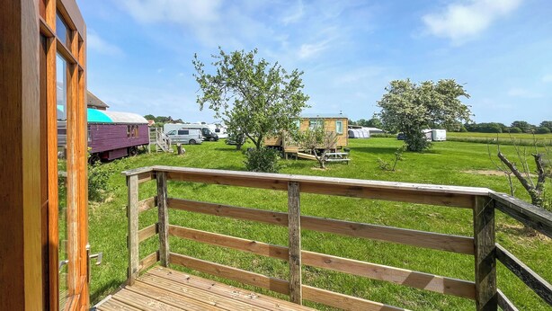 A wooden deck with a railing, a grassy field, and RVs in the background. - Ewe - Nice - UK51949 (Sutton on Sea, near Mablethorpe)
