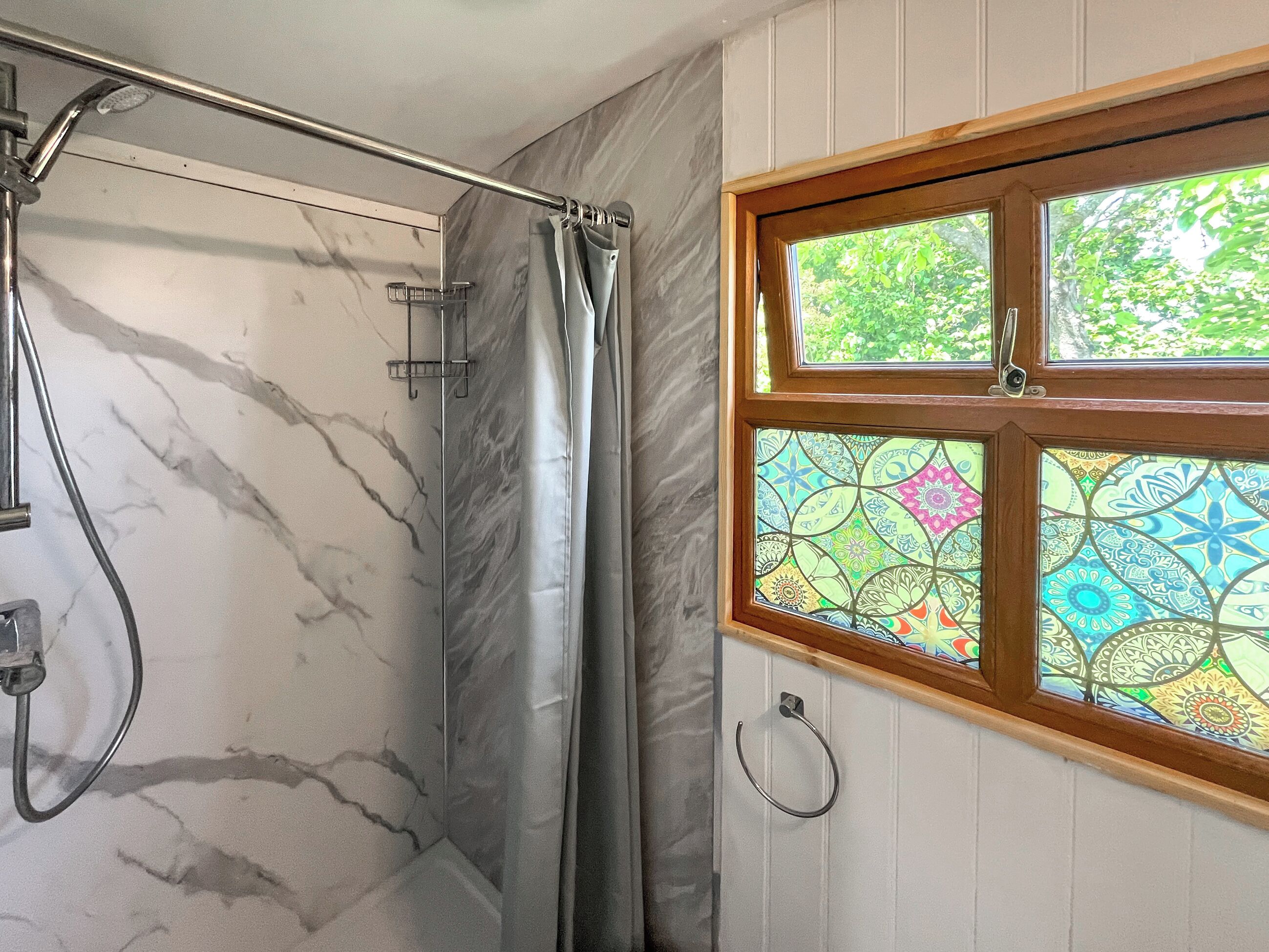 A bathroom with a shower, a window with stained glass, and a marble wall.