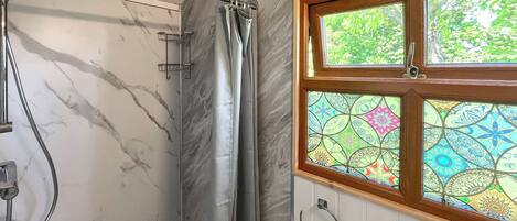 A bathroom with a shower, a window with stained glass, and a marble wall.