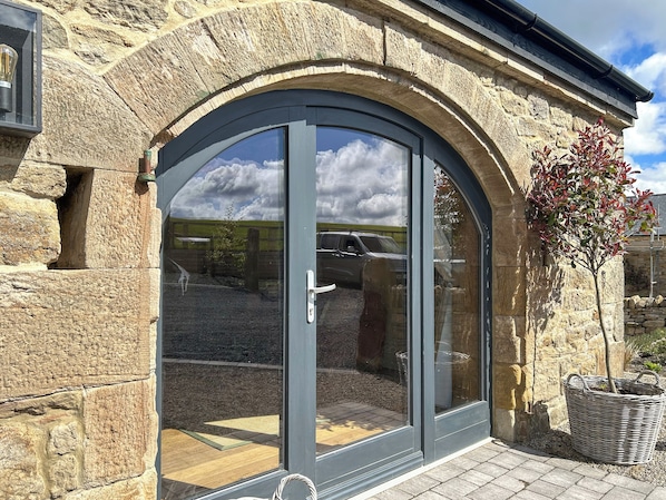 A stone building with a large arched glass door, a small tree, and a wicker basket.