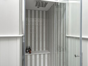 A bathroom with striped tiles, a shower area, and a shelf with toiletries.