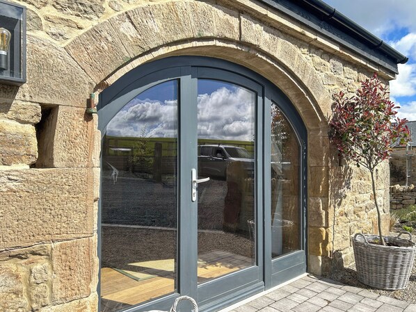 A stone building with a large arched glass door, a small tree, and a wicker basket.