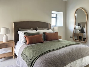 A neatly made bed with a quilted cover, a bedside lamp, and a nightstand with a drawer.