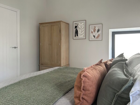 Un dormitorio con una cama, un armario de madera e dos láminas botánicas enmarcadas en la pared.