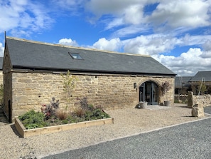 A stone building with a sloped roof, a small skylight, and a wooden planter with various plants.