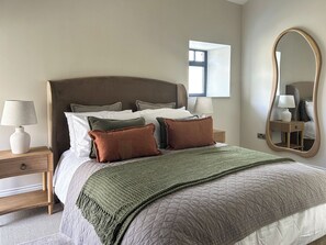 A neatly made bed with a quilted cover, a bedside lamp, and a nightstand with a drawer.