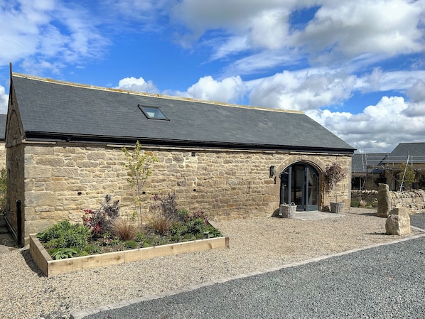 A stone building with a sloped roof, a small skylight, and a wooden planter with various plants.