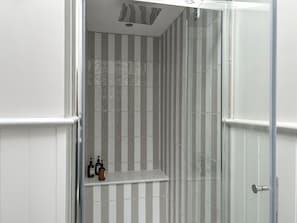 A bathroom with striped tiles, a shower area, and a shelf with toiletries.