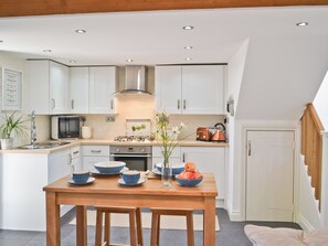 A modern kitchen with white cabinets, a wooden dining table, and a variety of kitchen appliances. - 1 bedroom accommodation in Plymouth (Plymouth)