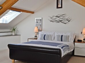 A bedroom with a sloped ceiling, a bed with striped bedding, bedside tables with lamps, a wall-mounted light fixture, and a potted plant. - 1 bedroom accommodation in Plymouth (Plymouth)